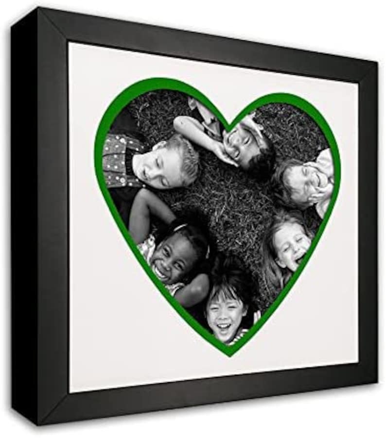 May include: Black and white photo of five children lying in a grassy field, their heads forming a heart shape with a green outline. The children are smiling and looking at the camera.