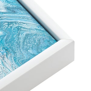 May include: Close-up of the corner of a white frame with a blue and white abstract painting inside.