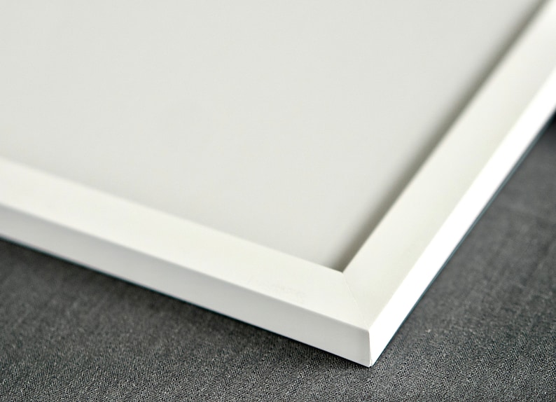 May include: A close-up view of a clean, white picture frame corner featuring a mitered joint. The frame has a smooth, matte finish and surrounds a plain, solid white interior surface, showcasing a simple and functional design for displaying art.