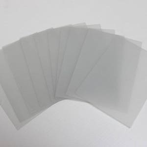 May include: A stack of ten clear plastic sheets, arranged in a fan shape, on a white background.