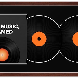 May include: A rectangular wall display featuring a dark brown wooden frame, a black mat, and two black vinyl records with orange center labels. A square insert on the left displays the white text "YOUR MUSIC, FRAMED" above a partial vinyl record.