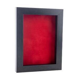 May include: A rectangular shadow box display frame featuring a dark charcoal black frame with a subtle wood grain texture and a vibrant, solid red velvet-like fabric backing. The deep frame design provides a recessed space for items.