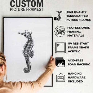 May include: A black picture frame with a white background and a black and white illustration of a seahorse. The frame is being hung on a white wall. The text "CUSTOM PICTURE FRAMES" is at the top of the image. The text "HIGH-QUALITY HANDCRAFTED PICTURE FRAMES" is on the right side of the image. The text "PROFESSIONAL FRAMING MATERIALS" is on the right side of the image. The text "UV RESISTANT FRAME GRADE ACRYLIC" is on the right side of the image. The text "ACID-FREE FOAM BACKING" is on the right side of the image. The text "HANGING HARDWARE INCLUDED" is on the right side of the image.