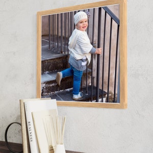 May include: A framed photograph of a young child wearing a white knitted hat and a white sweater, standing on a set of stairs and holding onto a metal railing. The child is looking at the camera and smiling.