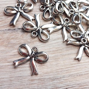 Op de afbeelding: Een stapel zilveren metalen strikbedels, elk met een lus om te bevestigen aan een ketting, armband of ander juweelproject.