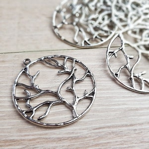 May include: Silver metal circle pendant with a tree branch design. The pendant is a circle with a tree branch design inside. The pendant is silver in color.