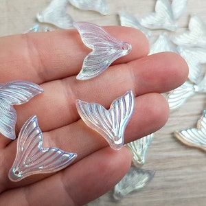 以下が含まれることがあります： 虹色のマーメイドテールのチャームのセット。透明なプラスチック製で、真珠のような光沢があります。チャームは魚の尾の形をしていて、上部に穴が開いており、ジュエリーやその他のクラフトに取り付けることができます。