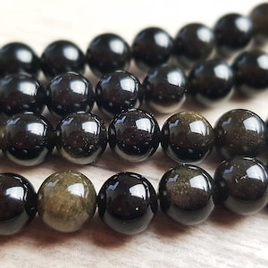 May include: A strand of black obsidian beads with a golden sheen. The beads are round and smooth, and they are strung on a clear thread.