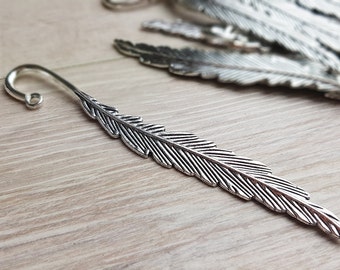Puede incluir: Marcapáginas de pluma de plata con un extremo curvado. El marcapáginas está detallado con líneas para parecerse a una pluma.