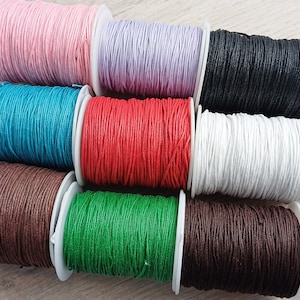 Könnte beinhalten: Sortiment von Spulen mit gewachstem Baumwollgarn in verschiedenen Farben, darunter rosa, Lavendel, schwarz, türkis, rot, weiß, braun, grün und dunkelbraun.