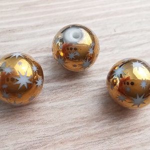Puede incluir: Tres cuentas de vidrio de color dorado con dise&ntilde;os de estrellas blancas. Las cuentas son redondas y tienen un acabado brillante.