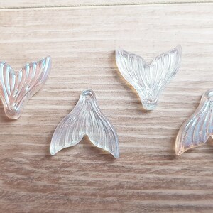 以下が含まれることがあります： ひもを通すための穴が付いた、虹色のマーメイドテールのチャームが4つ。チャームは透明なプラスチック製で、真珠のような光沢があります。