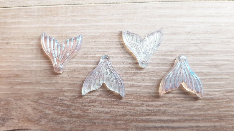 以下が含まれることがあります： ひもを通すための穴が付いた、虹色のマーメイドテールのチャームが4つ。チャームは透明なプラスチック製で、真珠のような光沢があります。