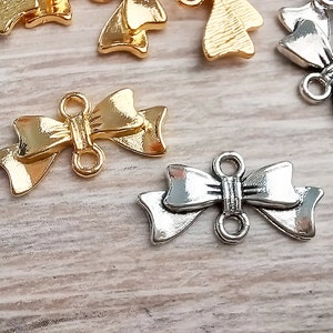 Op de afbeelding: Een close-up van twee gouden en twee zilveren metalen bedels in de vorm van een strik met twee lussen op elke bedel. De bedels liggen op een houten oppervlak.