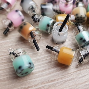 Op de afbeelding: Een verzameling miniatuur glazen potjes met kleurrijke vloeistoffen en zwarte rietjes. De potjes hebben een helder glazen lichaam en een zilveren deksel. De vloeistoffen zijn groen, roze, oranje en wit. De potjes zijn gerangschikt op een houten oppervlak.