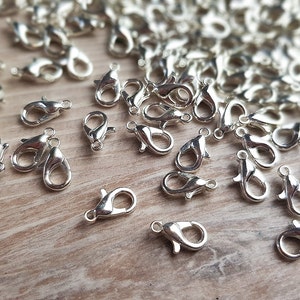 May include: A large quantity of silver-toned metal lobster claw clasps. The clasps are scattered on a wooden surface.
