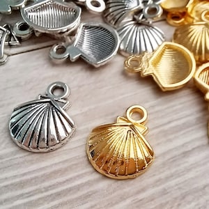 May include: A close-up of two silver and gold seashell charms. The charms are detailed with ridges and have a loop at the top for attaching to jewellery or other crafts.