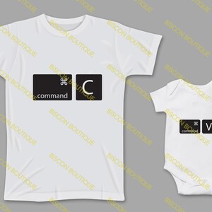 Puede incluir: Una camiseta blanca con un gráfico de tecla de teclado negro que dice "command" y "C". Un body blanco para bebé con un gráfico de tecla de teclado negro que dice "command" y "V".