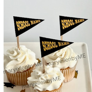 May include: Three cupcakes with white frosting and black and gold pennant flags that say "SCHOOL NAME" on top. The cupcakes are on a white plate with gold confetti.