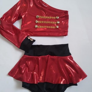 May include: A red and black two-piece outfit with a one-shoulder top and a ruffled skirt. The top has gold trim and buttons.