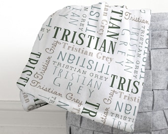 May include: White baby blanket with a repeating pattern of the name "Tristian" in various shades of green and brown.