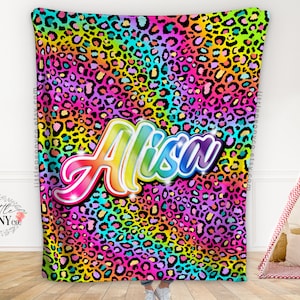 Puede incluir: Una manta de forro polar con estampado de leopardo arcoíris con el nombre "Alisa" en una fuente arcoíris.
