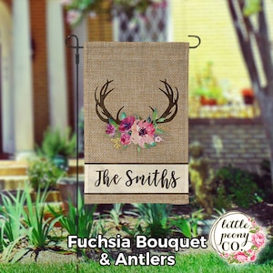 May include: A burlap garden flag featuring a floral design with fuchsia and pink flowers, brown antlers, and the text "The Smiths". The flag also includes the text "Fuchsia Bouquet & Antlers".