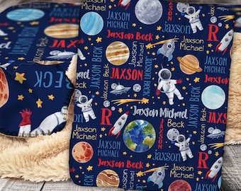 Pode incluir: Um cobertor azul e branco para bebé com tema espacial. Apresenta planetas, estrelas, foguetes e astronautas. O cobertor tem o nome "Jaxson Michael Beck" repetido por toda a sua superfície.