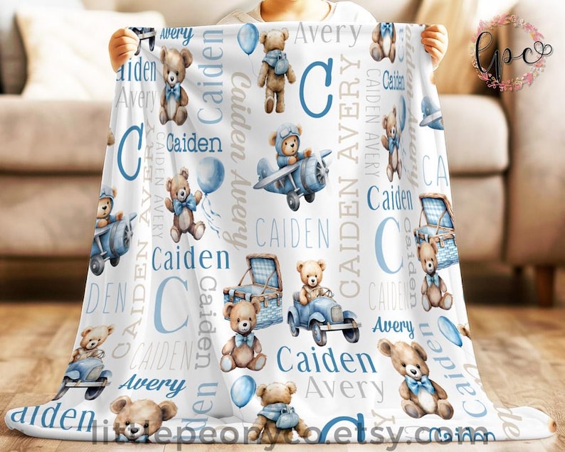 May include: White baby blanket featuring teddy bears, balloons, and the names "Caiden" and "Avery" in blue and gray. The blanket has a repeating pattern of teddy bears in various vehicles and poses.