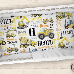 May include: A white cot sheet with a yellow and grey construction vehicle pattern. The sheet features the name "Henry" repeated throughout the design.