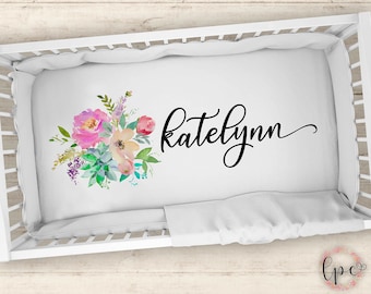 Puede incluir: Sábana de cuna blanca con un diseño floral de acuarela y el nombre "Katelyn" escrito en cursiva negra.