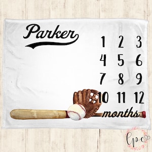Op de afbeelding: Een witte babydeken met een baseballthema. Het heeft een honkbalknuppel, handschoen en bal. De deken is gepersonaliseerd met de naam "Parker" en de nummers 1-12 om de groei van een baby bij te houden.
