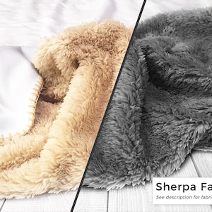 May include: A close-up of a blanket with three distinct textures and colors. The blanket features a white, smooth fabric, a tan, fluffy sherpa, and a gray, fluffy sherpa. The text "Sherpa Fabric" is visible.
