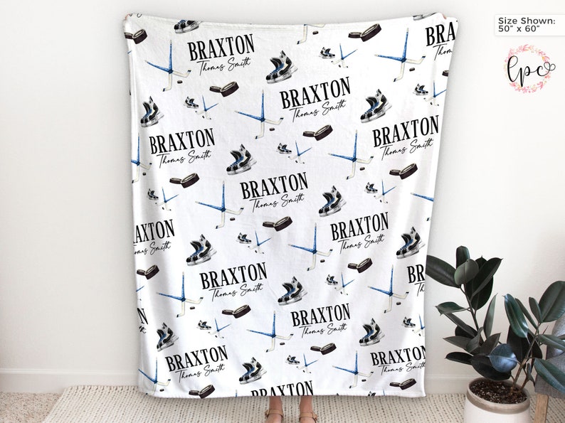May include: White fleece blanket with a repeating pattern of hockey skates, sticks, and pucks. The text "BRAXTON Thomas Smith" is repeated throughout the pattern. The blanket is 50 inches by 60 inches.