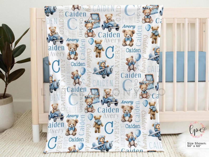 May include: A white baby blanket with a repeating pattern of teddy bears, airplanes, cars, and the names "Caiden" and "Avery" in blue. The blanket is displayed on a crib and measures 50 x 60 inches.