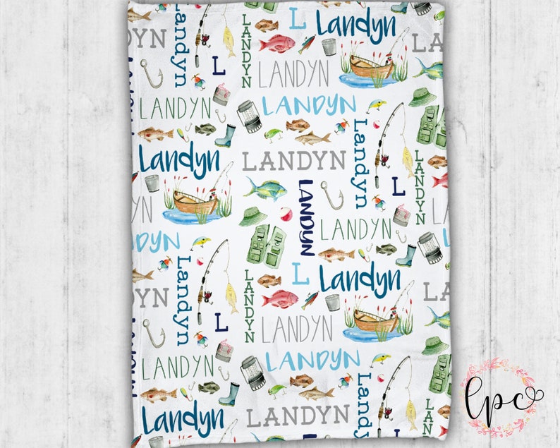 Puede incluir: Una manta de beb&eacute; blanca con un patr&oacute;n repetido de ilustraciones de tem&aacute;tica de pesca en azul y verde. El nombre "Landyn" se repite en todo el patr&oacute;n.