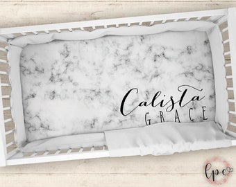 May include: White crib sheet with a marble pattern and the name "Calista Grace" printed in black cursive.