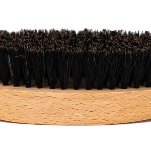 May include: A wooden-handled brush with black bristles. The brush is oval-shaped and has a natural wood finish.