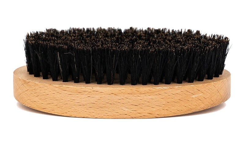 May include: A wooden-handled brush with black bristles. The brush is oval-shaped and has a natural wood finish.