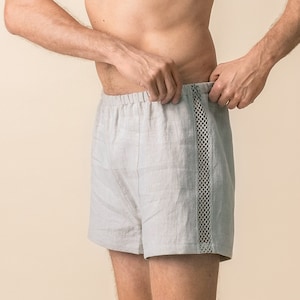 Könnte beinhalten: Ein Mann trägt hellgraue Leinenhosen mit schwarzem und weißem Besatz. Die Hose hat einen Kordelzug.