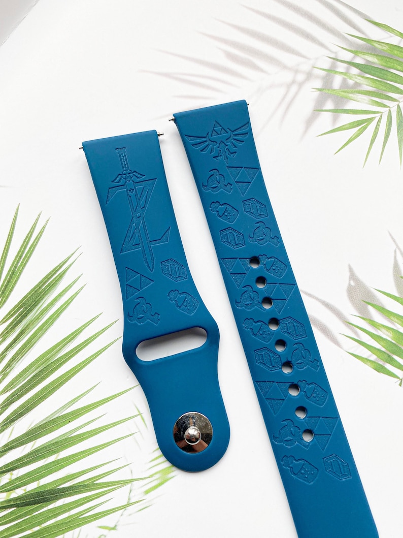 Op de afbeelding: Twee blauwe siliconen horlogebandjes met een Zelda-thema. E&eacute;n bandje heeft een zwaard en het andere bandje heeft de Triforce en andere Zelda-symbolen.