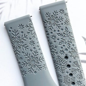 May include: Two gray silicone watch bands with a snowflake pattern. The bands are embossed with snowflakes and other small designs.
