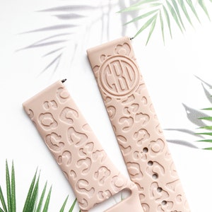 May include: Two pink silicone watch bands with a leopard print design. One band has a monogrammed circle with the initials "CBO" in the center.