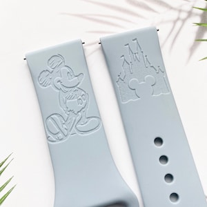 May include: Two light blue silicone watch straps with engraved designs. One strap features Mickey Mouse and the other features the Disney castle with Mickey Mouse's head in front of it.