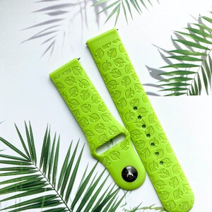 May include: Two green silicone watch bands with a leaf pattern. The bands are designed for smartwatches and have a buckle closure.