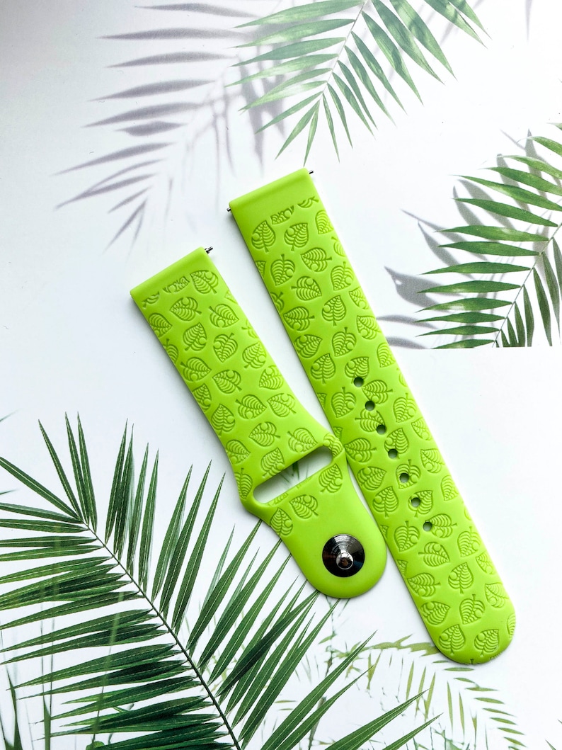 May include: Two green silicone watch bands with a leaf pattern. The bands are designed for smartwatches and have a buckle closure.
