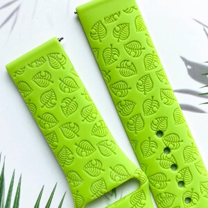May include: A bright green silicone watch band with a repeating pattern of green leaves. The band is designed for a smartwatch.