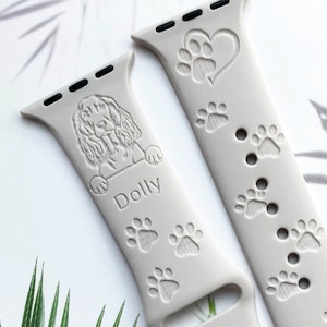 K&ouml;nnte beinhalten: Ein graues Silikonarmband f&uuml;r die Apple Watch mit einem Pfotenabdruck-Design und einem Herz mit einem Pfotenabdruck darin. Das Armband ist mit einem Hundeportrait und dem Namen "Dolly" personalisiert.