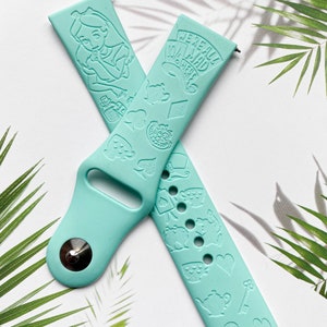 May include: A light blue silicone Apple Watch band with a white Alice in Wonderland design. The band features a variety of characters and symbols from the story, including Alice, the Mad Hatter, the Cheshire Cat, and playing cards. The text "We're all mad here" is printed on the band.
