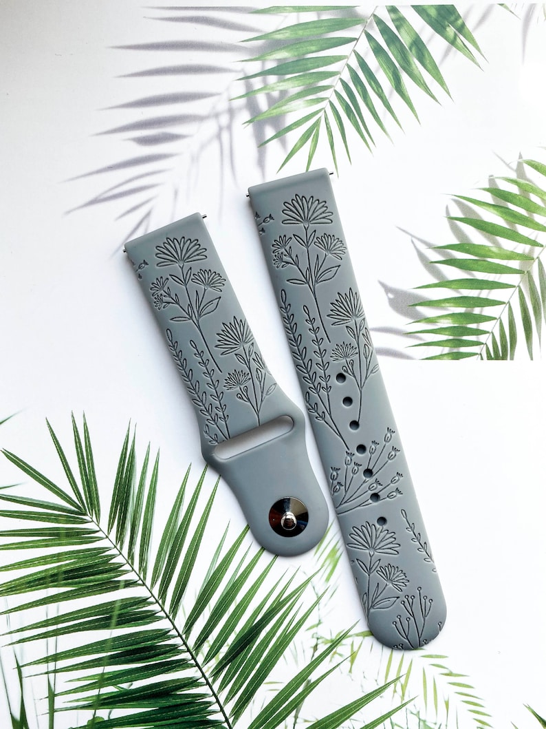 May include: Two gray silicone watch bands with a floral design. The bands are embossed with a delicate floral pattern.